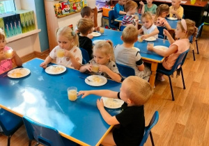 Dzieci siedzą przy stoliku, piją sok i jedzą ryż ze startymi jabłkami