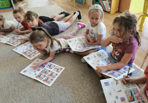 Grupa dzieci siedzi na dywanie i wykonuje zadania w książce