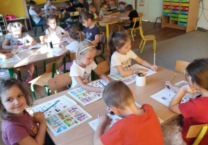 Grupa dzieci siedzi przy stole i pracuje w książkach