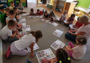 Dzieci siedzą na dywanie i słuchają poleceń nauczycielki