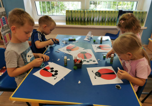 Dzieci siedząc przy stoliku wykonują prace plastyczne