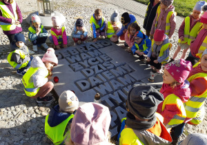 Dzieci otaczają tablicę upamiętniającą ofiary obozu przy ulicy Przemysłowej