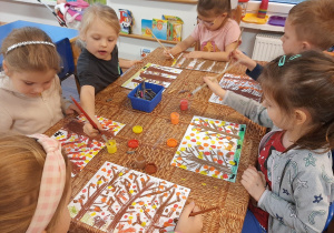Dzieci siedzą przy stoliku i malują jesienne drzewa