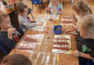 Dzieci siedzą przy stoliku i malują jesienne drzewa