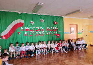 Dzieci siedzą na tle patriotycznej dekoracji