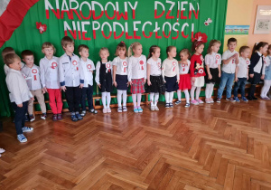 Dzieci śpiewają hymn Polski w postawie na baczność.