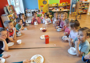 Dzieci siedzą przy stole i degustują herbatkę.