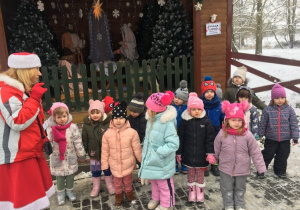 Grupa dzieci stoi przed szopką bożonarodzeniową