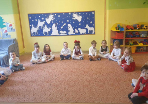 Dzieci siedzą w półkolu czekając na rozpoczęcie spotkania