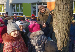 Grupa dzieci stoi przy drzewie.