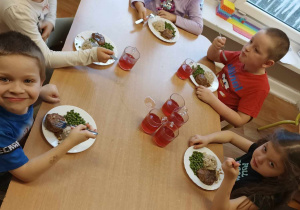 Grupa dzieci siedzi przy stoliku i je.