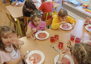 Grupa dzieci siedzi przy stoliku i je.