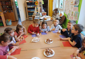 Dzieci siedzą przy stole i degustują smakołyki.