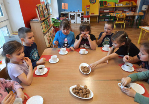 Dzieci siedzą przy stole i jedzą ,,włoskie" ciasteczka.