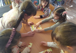 Grupa dzieci układa puzzle z dinozaurem