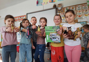Dzieci prezentują figurki dinozaurów i książkę