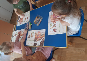 Dzieci wypełniają karty pracy z dinozaurami
