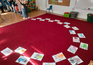Wykonane przez dzieci ślady stóp dinozaurów leżą rozłożone na dywanie w klasie