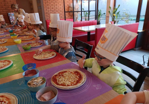 Grupa dzieci nakłada składniki na pizzę.
