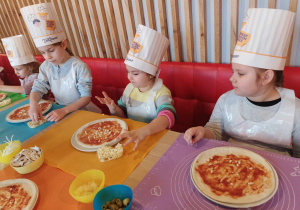 Grupa dzieci nakłada składniki na pizzę.