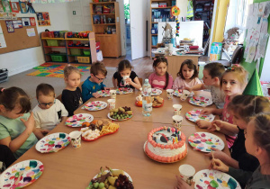 Dzieci siedzą przy stole i degustują słodkości.