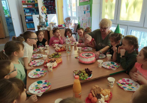Dzieci siedzą przy stole i degustują słodkości.