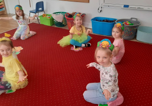 Dzieci siedzą przy kwiatkach ułożnych na dywanie