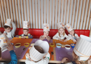 Dzieci siędzą przy stoliku w czapkach kucharskich