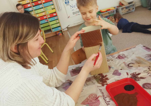 Chłopiec wspólnie z nauczycielką malują elementy wiatraka