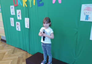 Dziewczynka stoi na scenie trzymając w rękach mikrofon