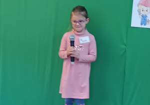 Dziewczynka stoi na scenie trzymając w rękach mikrofon
