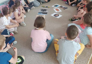 Dzieci siedzą na dywanie i oglądają ilustracje.