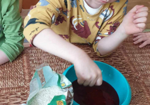 chłopiec wsypuje ryż do wody zabarwionej bibułą