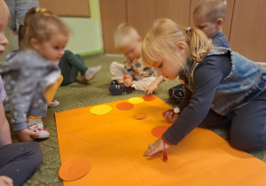 Dzieci naklejają na papierowe drzewo kolorowe kropki