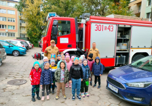 Dzieci pozują do zdjęcia ze strażakami na tle wozu strażackiego