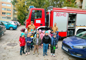 Dzieci pozują do zdjęcia ze strażakami na tle wozu strażackiego