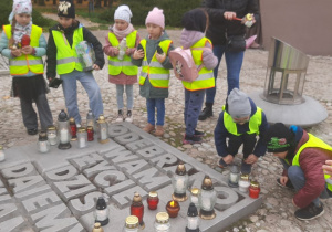 Dzieci stawiają zapalone znicze