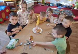 Grupa dzieci degustuje przy stoliku miodek.