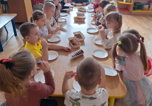 Dzieci siedą przy stole i spożywają słodycze.