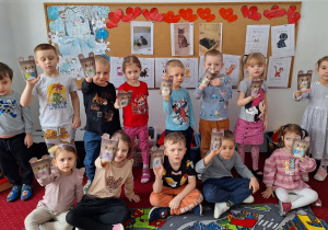 Dzieci stoją na dywanie i pokazują zrobione przez siebie koty.