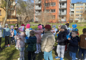 Dzieci słuchają nauczycielki objaśniającej zasady obowiązujące podczas sprzątania ogrodu przedszkolnego