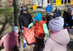 Dzieci wrzucają śmieci do worka trzymanego przez kolegę