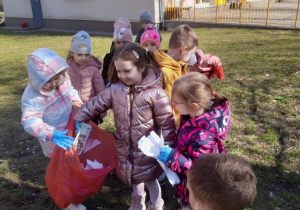 Dziewczynka wrzuca śmieci do worka trzymanego przez koleżankę