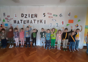 Dzieci ustawione w rzędzie podnoszą do góry lewą rękę