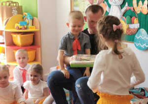 Dziewczynka stoi na dywanie i otrzymuje prezent od zajączka"