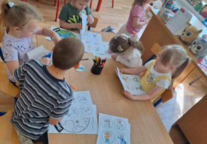 Grupa dzieci siedzi przy stole i koloruje obrazek kuli ziem