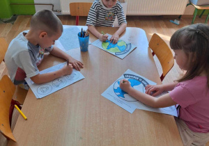 Grupa dzieci siedzi przy stole i koloruje obrazek kuli ziemskiej