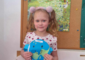 Dziewczynka pozuje do zdjęcia trzymając obrazek kuli ziemskiej
