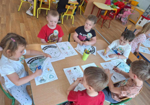 Grupa dzieci siedzi przy stole i koloruje obrazek kuli ziemskiej