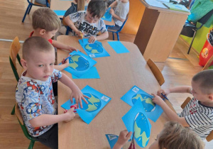 Grupa dzieci siedzi przy stole i wycina obrazek kuli ziemskiej